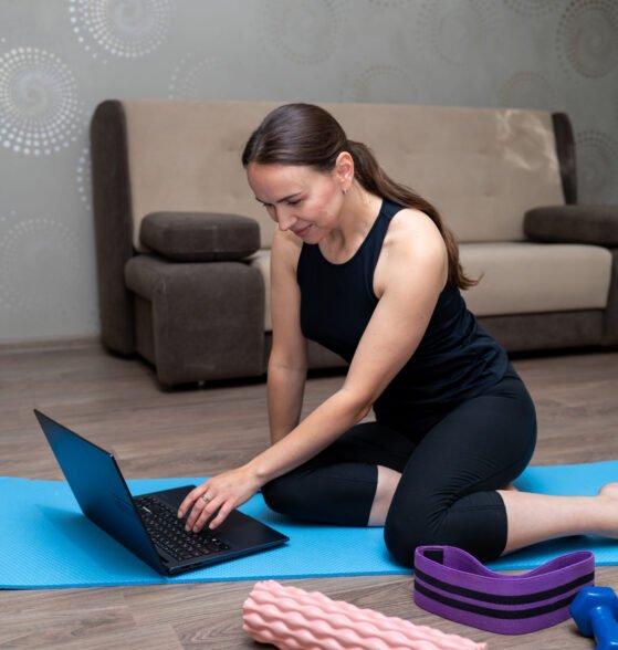 Young woman exercising at home with dumbbells, foam roller, resistance band and yoga mat, following online fitness program, healthy lifestyle