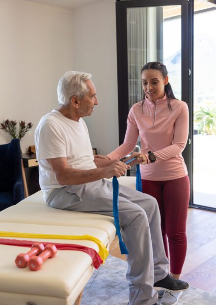 Biracial female physiotherapist helping senior man to exercise with resistance bands. Physiotherapy and rehabilitation concept