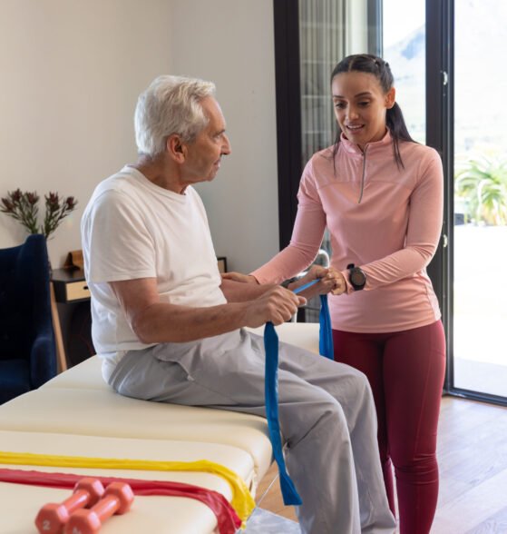Biracial female physiotherapist helping senior man to exercise with resistance bands. Physiotherapy and rehabilitation concept