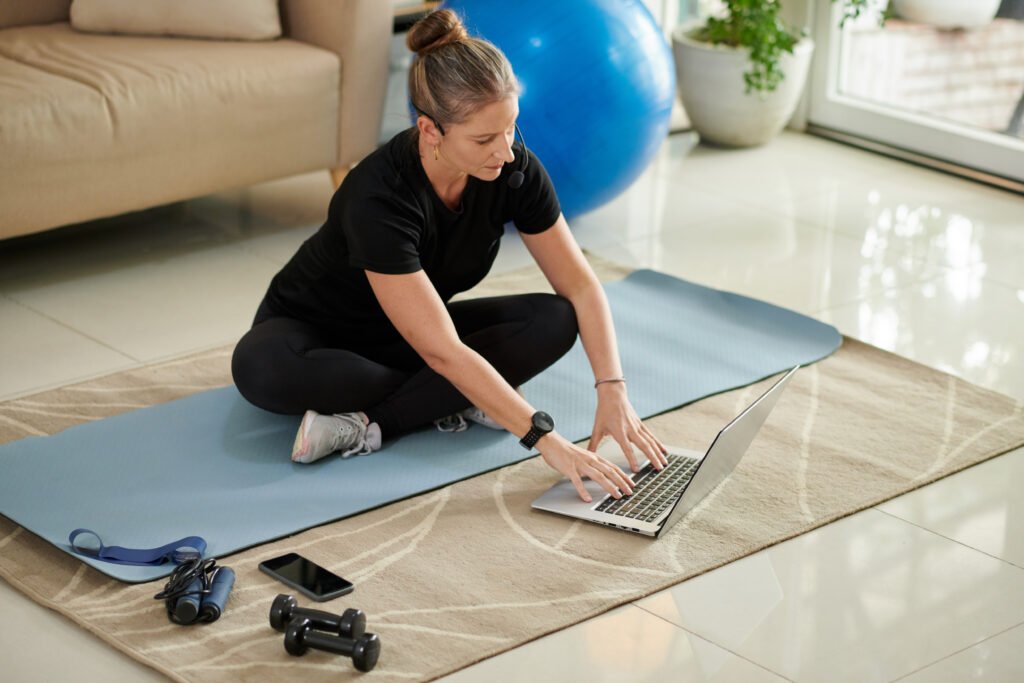 Woman attending a virtual physiotherapy session at home using a laptop on a yoga mat